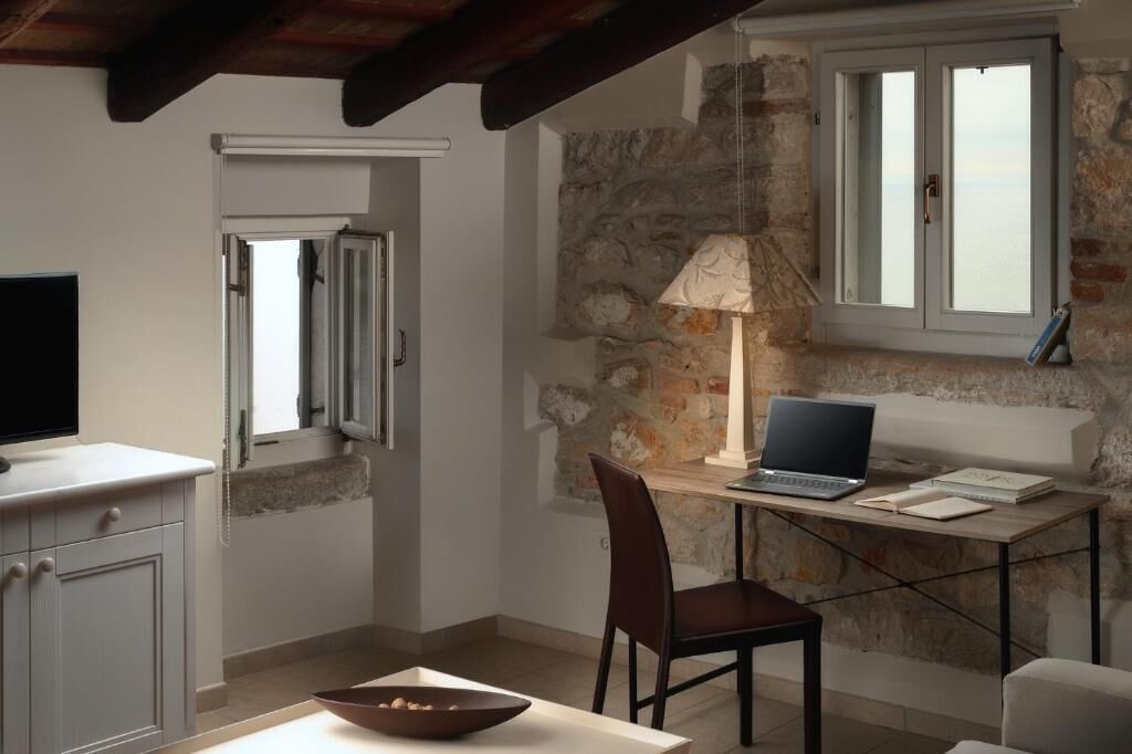 A cozy room with a stone wall, a wooden desk with a laptop, a lamp, and a bowl on the table.