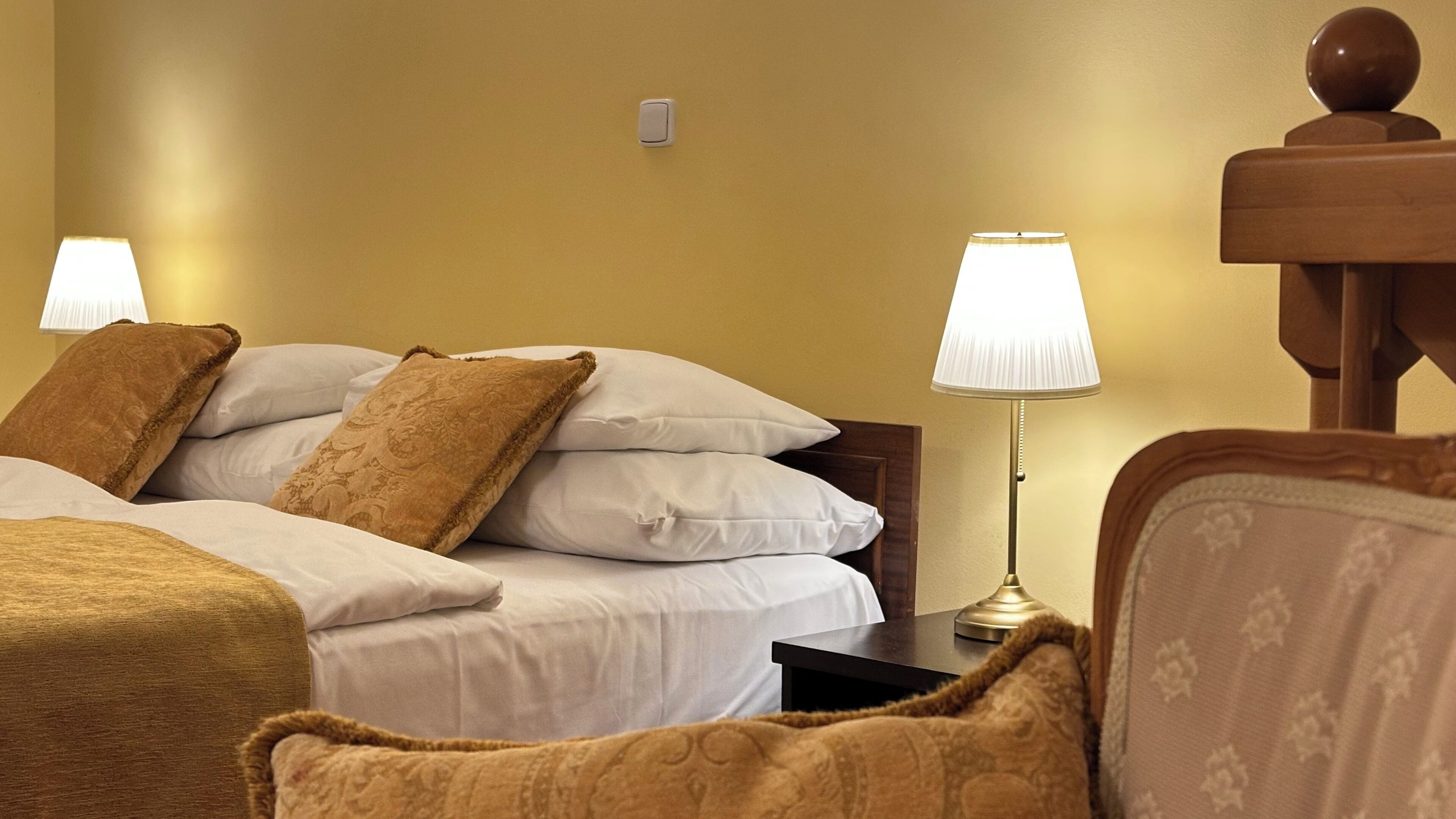 A hotel room with a bed, two bedside lamps, a nightstand, and a wooden chair.