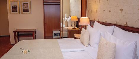 A hotel room with a neatly made bed, a bedside table with a lamp, and a mirror reflecting the room. There are two framed pictures on the wall.