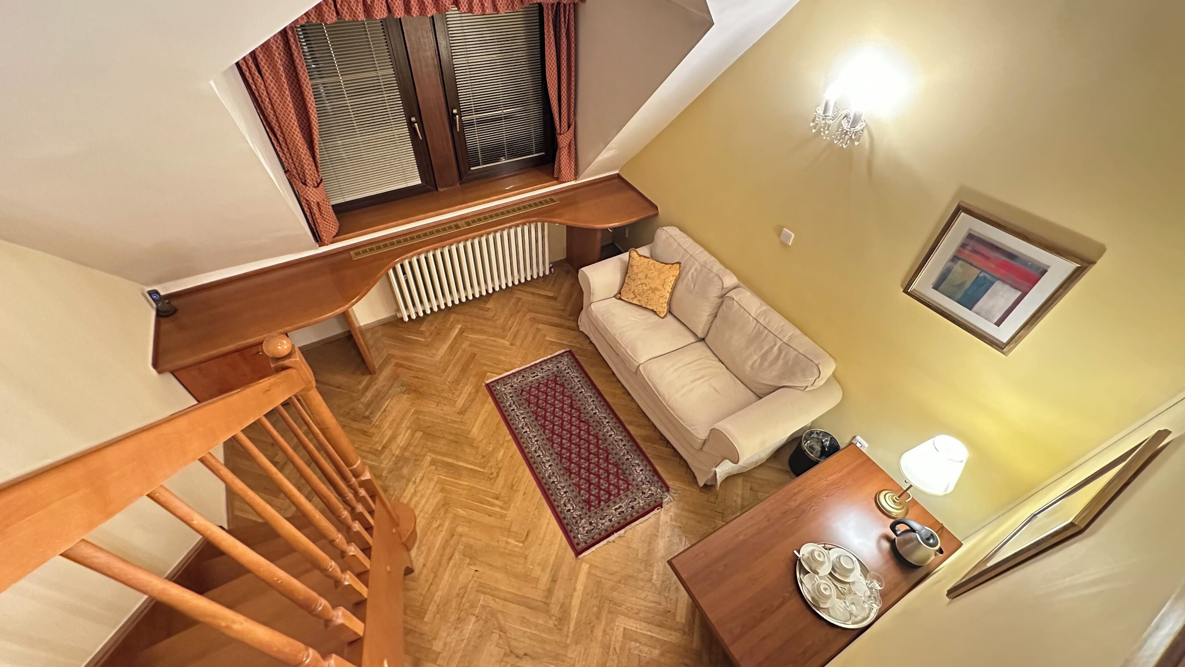 A staircase leading to a living area with a sofa, a radiator, a patterned rug, and a table with a tray of cups and a kettle.