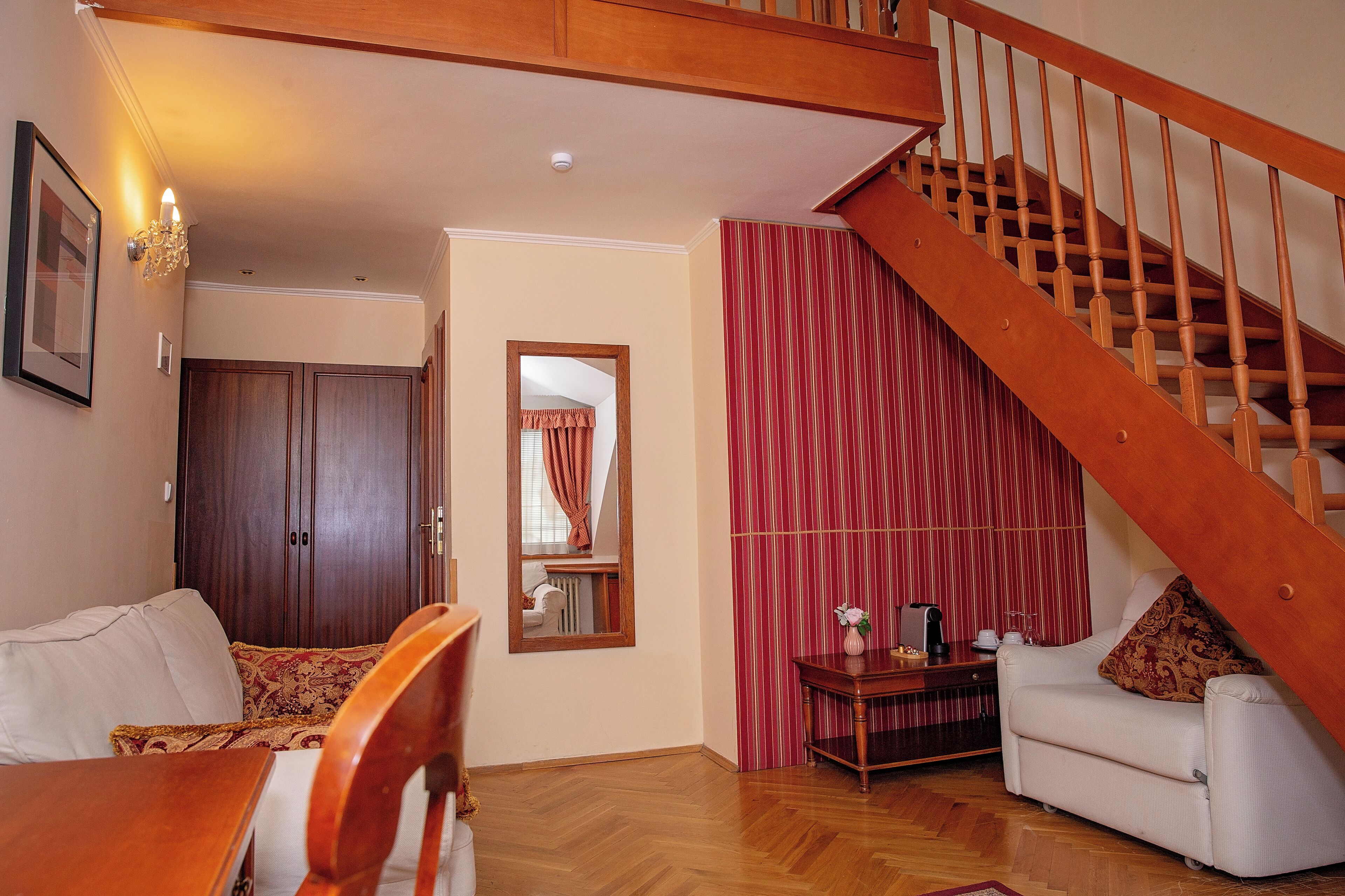 A living room with a wooden staircase, a sofa, a dining table, and a mirror.