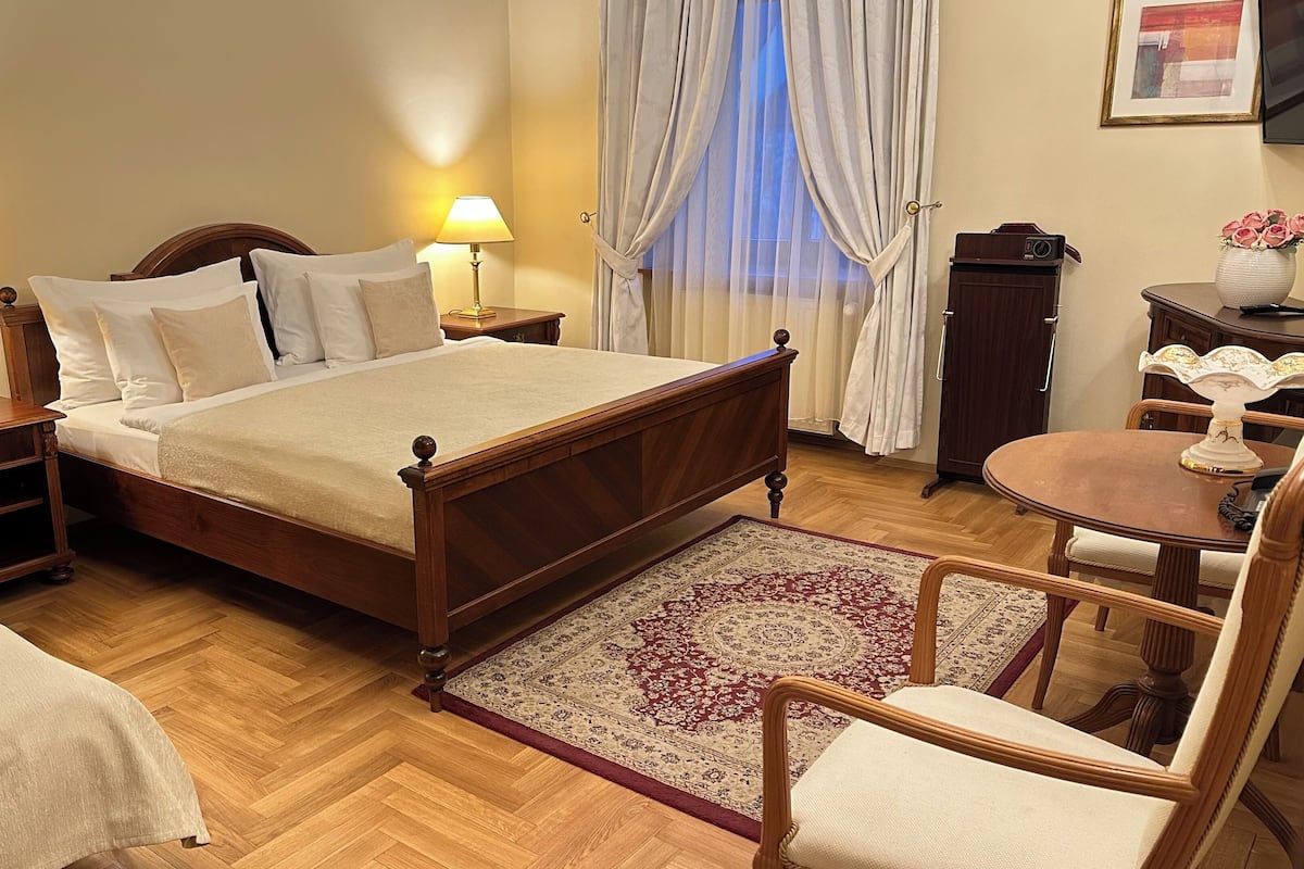 A neatly arranged bedroom with a wooden bed, two bedside tables with lamps, a small round table with a vase, and a chair.