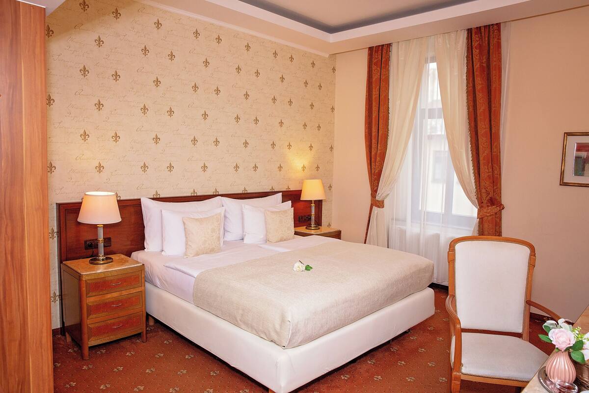 A hotel room with a large bed, two bedside tables with lamps, a wooden chair, and a floral-patterned wallpaper.
