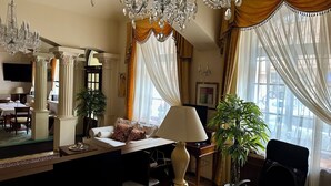 Een stijlvol ingerichte hotelkamer met een zithoek, een grote kroonluchter, een bank met een tafeltje en een bureau met een lamp en papieren.