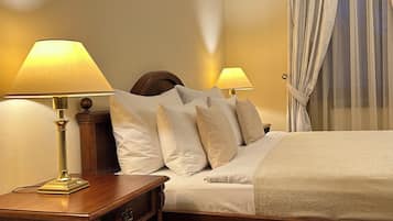 Una cama cuidadosamente tendida con sábanas blancas y varios almohadones, con dos lámparas de noche sobre mesitas de madera.