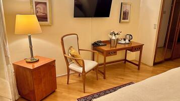 Una habitación de hotel con un escritorio de madera, una silla, un televisor montado en la pared, una lámpara y una cama.