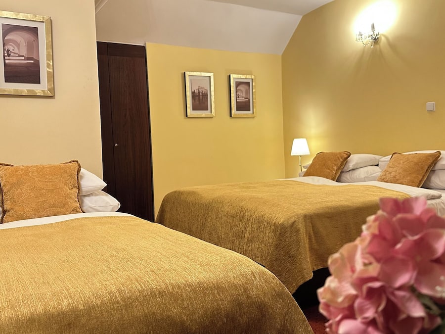 Habitación de hotel con dos camas, cada una con cubrecama marrón y almohadas blancas. Hay cuadros enmarcados en la pared, una lámpara y una puerta.