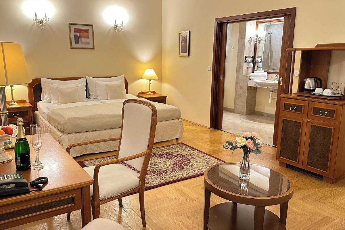 A hotel room with a bed, bedside tables, a desk with a telephone, a chair, a small table with a vase, and a cabinet with drawers.