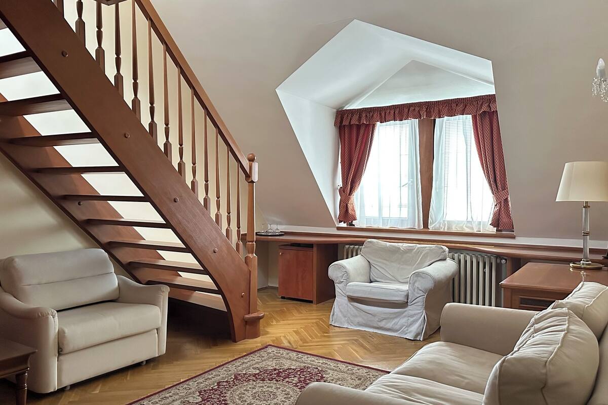 A cozy living room with a wooden staircase, a sofa, a chair, and a window with curtains.