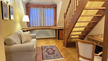 Una sala acogedora con un sofá, un tapete estampado, una silla de madera, un radiador y una escalera.