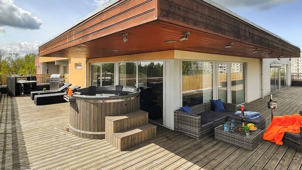Een modern terras buiten met een hottub, zitgedeelte en een barbecue.