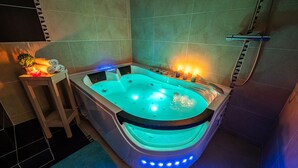 Een moderne spa met een verwarmd bad, een houten kruk met handdoeken en een klein tafeltje met kaarsen.