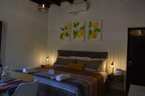 A hotel room with a bed, bedside tables, a desk with a chair, and wall-mounted artwork.