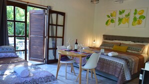 Quarto com cama, mesa e cadeiras, janela com persianas e obras de arte na parede.