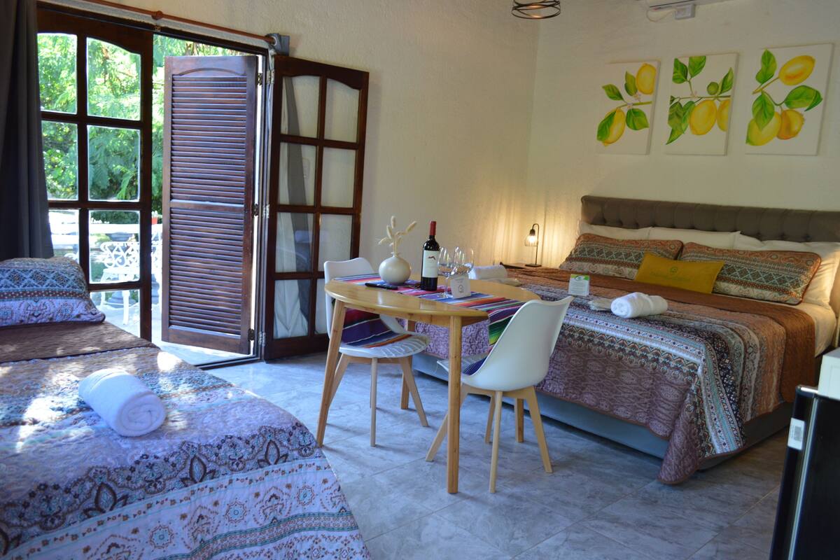 Un dormitorio con cama, una mesa y sillas, una ventana con contraventanas y obras de arte en la pared.