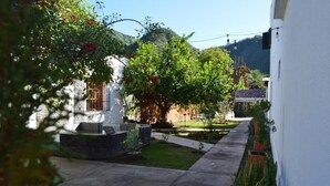 Um pátio com um edifício branco, um banco de pedra e um pequeno jardim com uma árvore e flores.