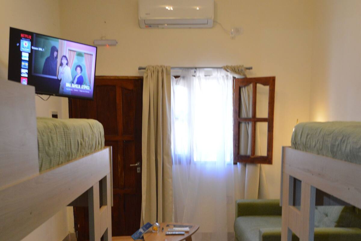 Una habitación con literas, televisión, aire acondicionado y una mesita.