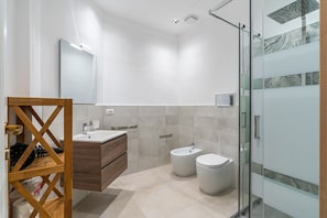 Un baño moderno con tocador de madera, un bidé, un inodoro y una cabina de ducha de vidrio.
