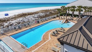 Ein Swimmingpool mit Rutsche, umgeben von Liegestühlen und Palmen, mit Strand und Meer im Hintergrund.