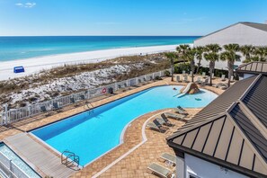 Ein Swimmingpool mit Rutsche, umgeben von Liegestühlen und Palmen, mit Strand und Meer im Hintergrund.