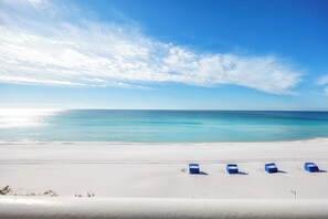 Una playa con arena blanca y un cielo azul despejado. Hay tres sillas de playa azules en línea sobre la arena.