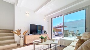 A modern living room with a flat-screen TV, a wooden console, a round coffee table, and a large sliding glass door leading to an outdoor area. - Villa with private pool, roof terrace and BBQ (Los Alcazares)