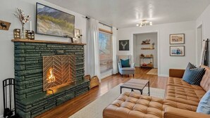 A living room with a stone fireplace, a leather sofa, and a large painting on the wall. - The Gray Pine | Hot Tub, Fire Pit, Office + A/C (Flagstaff)