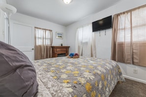 Um quarto com uma cama, uma escrivaninha, uma televisão e uma janela com cortinas.