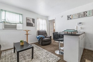 Um espaço compacto com cozinha compacta, uma poltrona cinza, uma mesa pequena e um vaso com planta.
