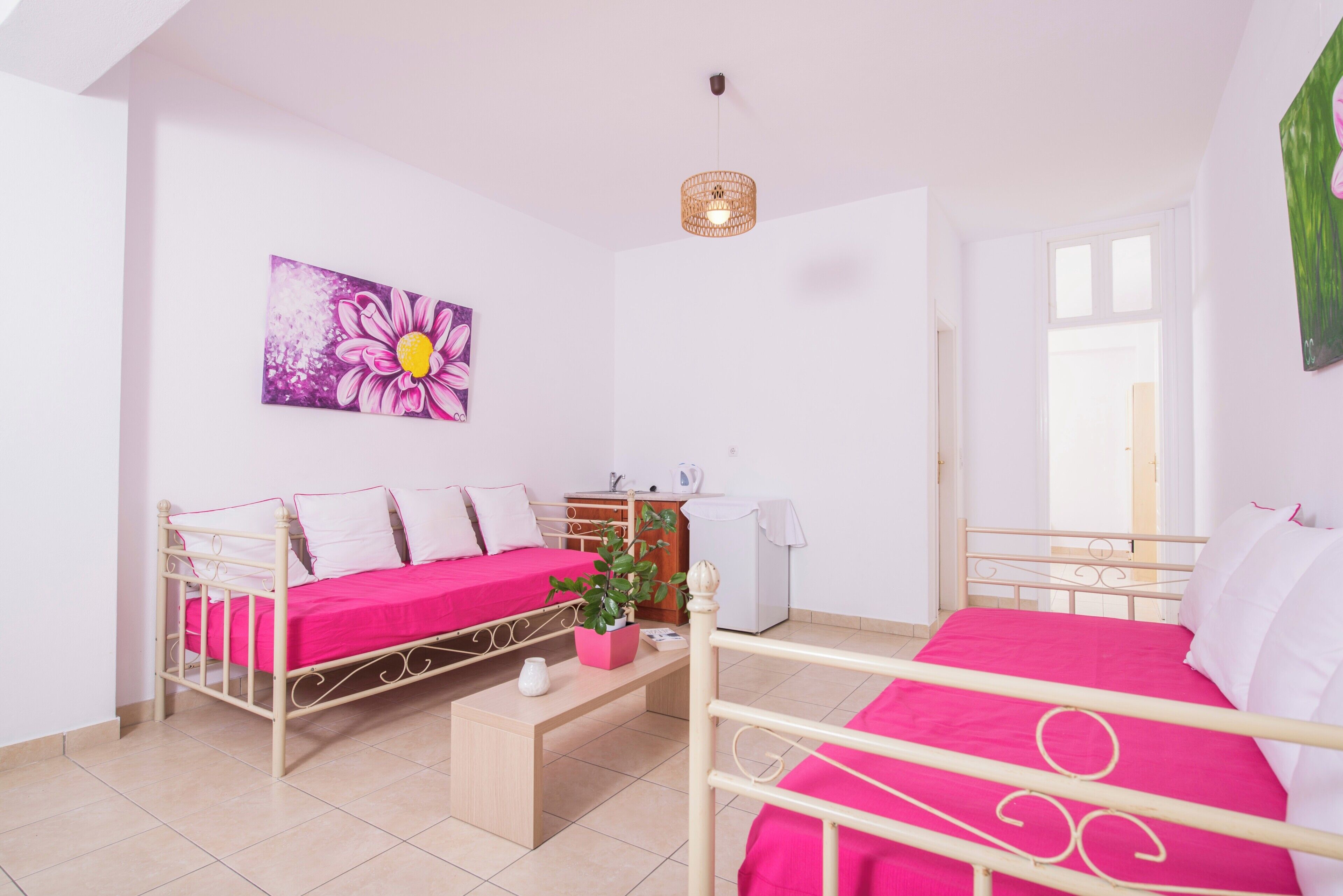 A room with two beds, a small table, a plant, and a painting on the wall.