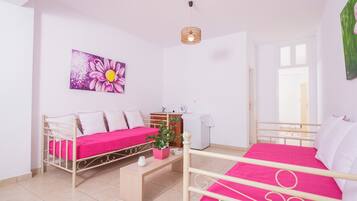 A room with two beds, a small table, a plant, and a painting on the wall.