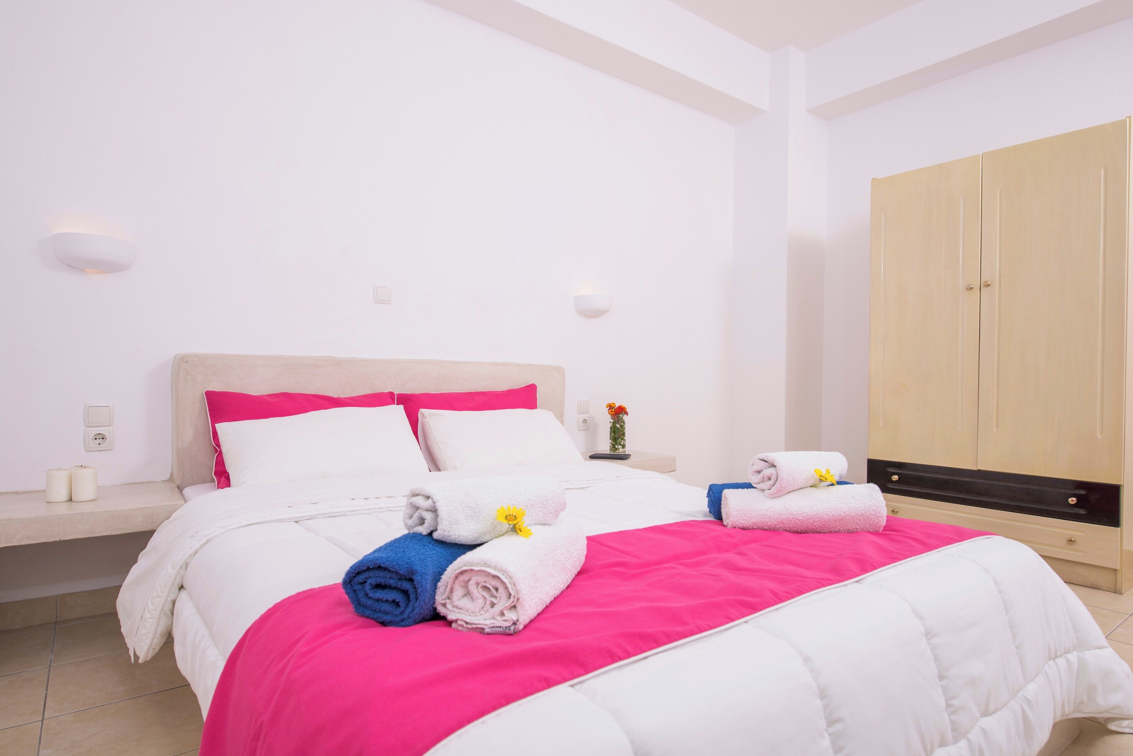 Habitación de hotel con cama, mesita de noche, armario y lámpara fijada a la pared.