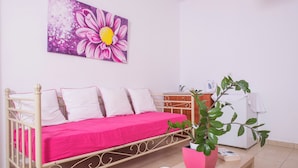 Una habitación con una cama, una planta en maceta, un florero blanco y un cuadro en la pared.