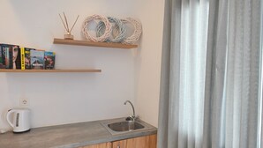 A kitchenette with a sink, wooden cabinets, and bookshelves with books. - 1-bed Apt at Hotel, Near Perivolos Black Beach (Santorini)