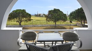 A balcony with two wicker chairs and a table, overlooking a grassy area with trees and a fence. - 1-bed Apt at Hotel, Near Perivolos Black Beach (Santorini)