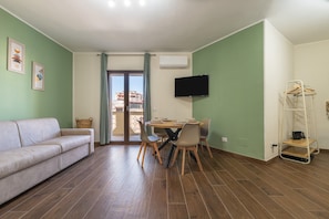 A room with a sofa, dining table, chairs, a TV, and a balcony view.