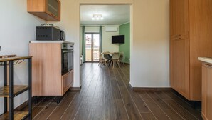 A kitchen with a microwave, oven, and wooden cabinets. There is a dining area with chairs and a table. - Apartment 'Sa Domixedda' in Quartu Sant'Elena – Central, Renovated, Near Poetto Beach (Quartu Sant'Elena)