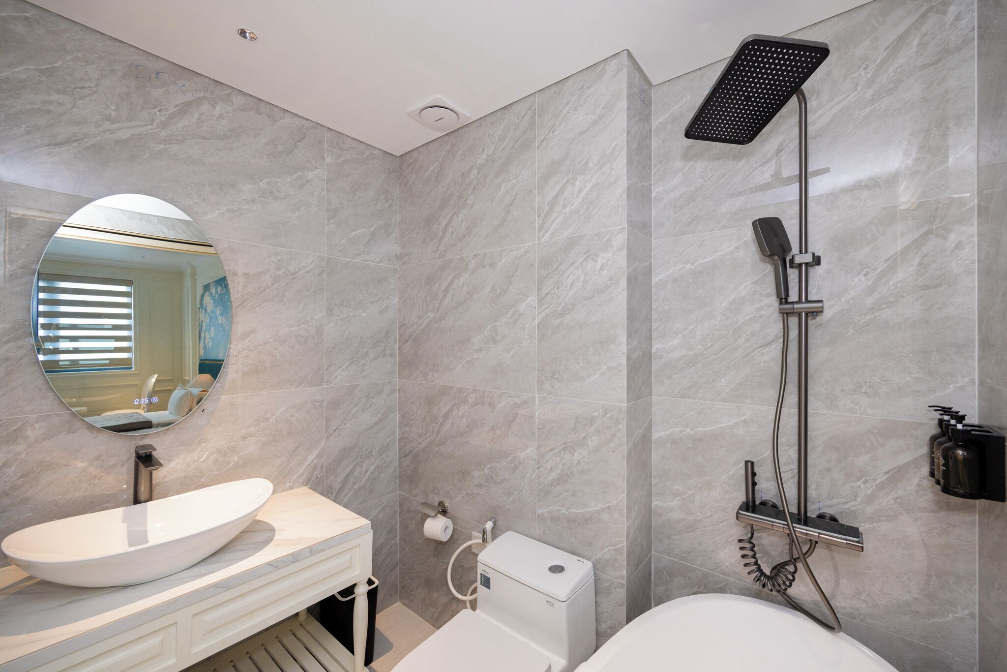 A modern bathroom with a large oval sink, a handheld showerhead, and a toilet.