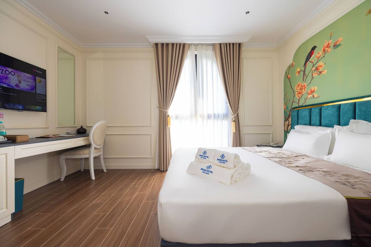 A hotel room with a large bed, a desk, a chair, and a TV on the wall.