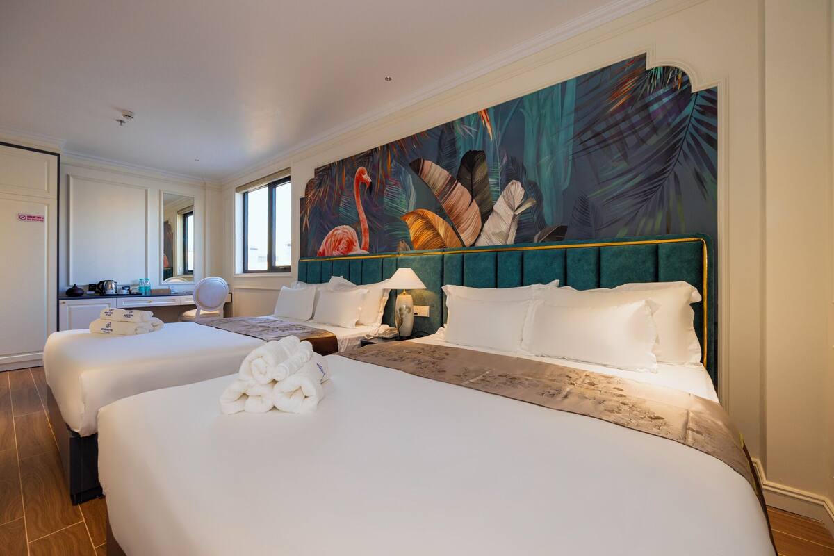 A hotel room with two beds, a large tropical mural, and a view of the city.