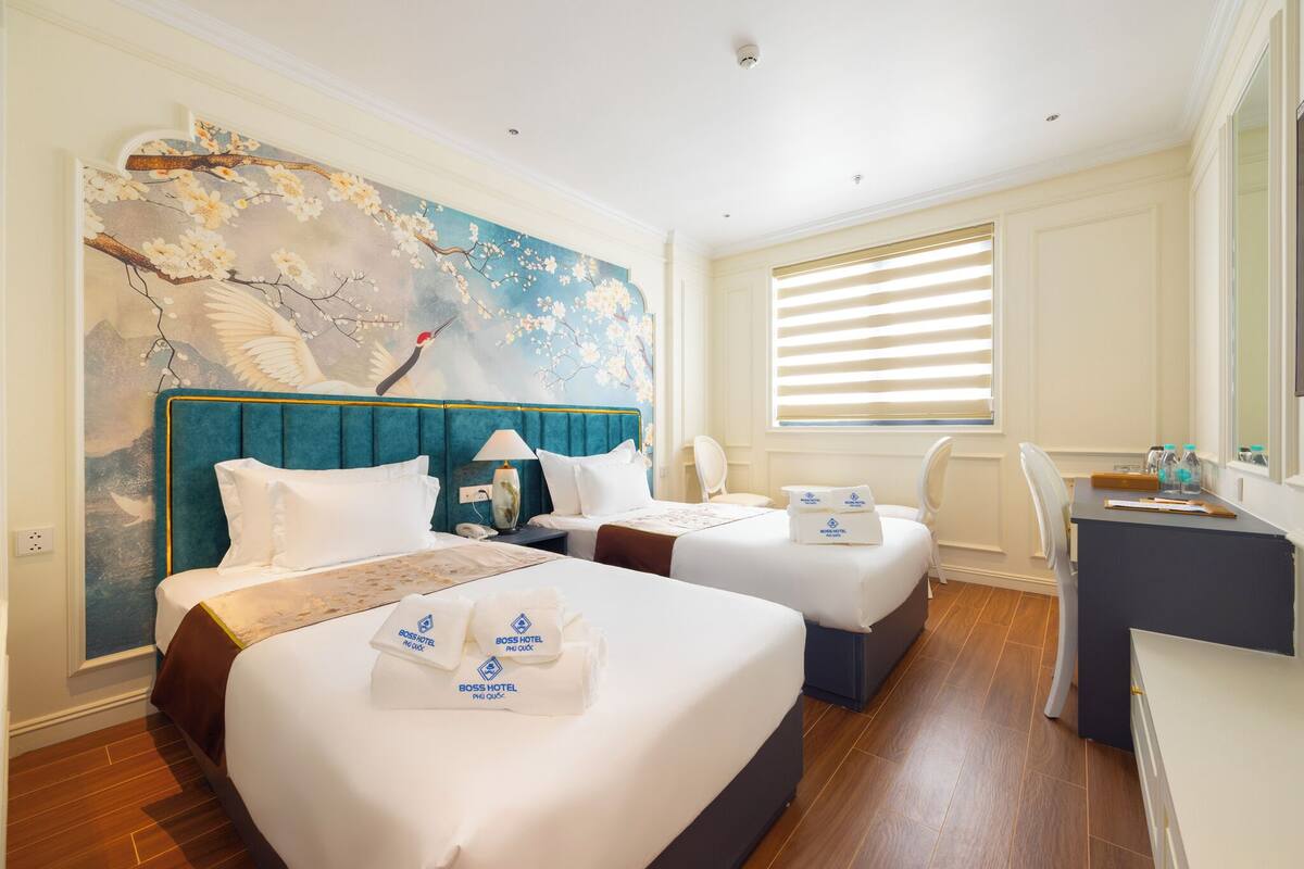 A hotel room with two beds, a desk, and a large window with blinds.