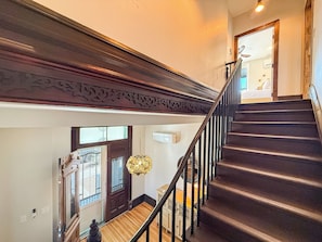 Una escalera con escalones oscuros y barandal de madera, que conduce a un rellano con una puerta y una ventana.