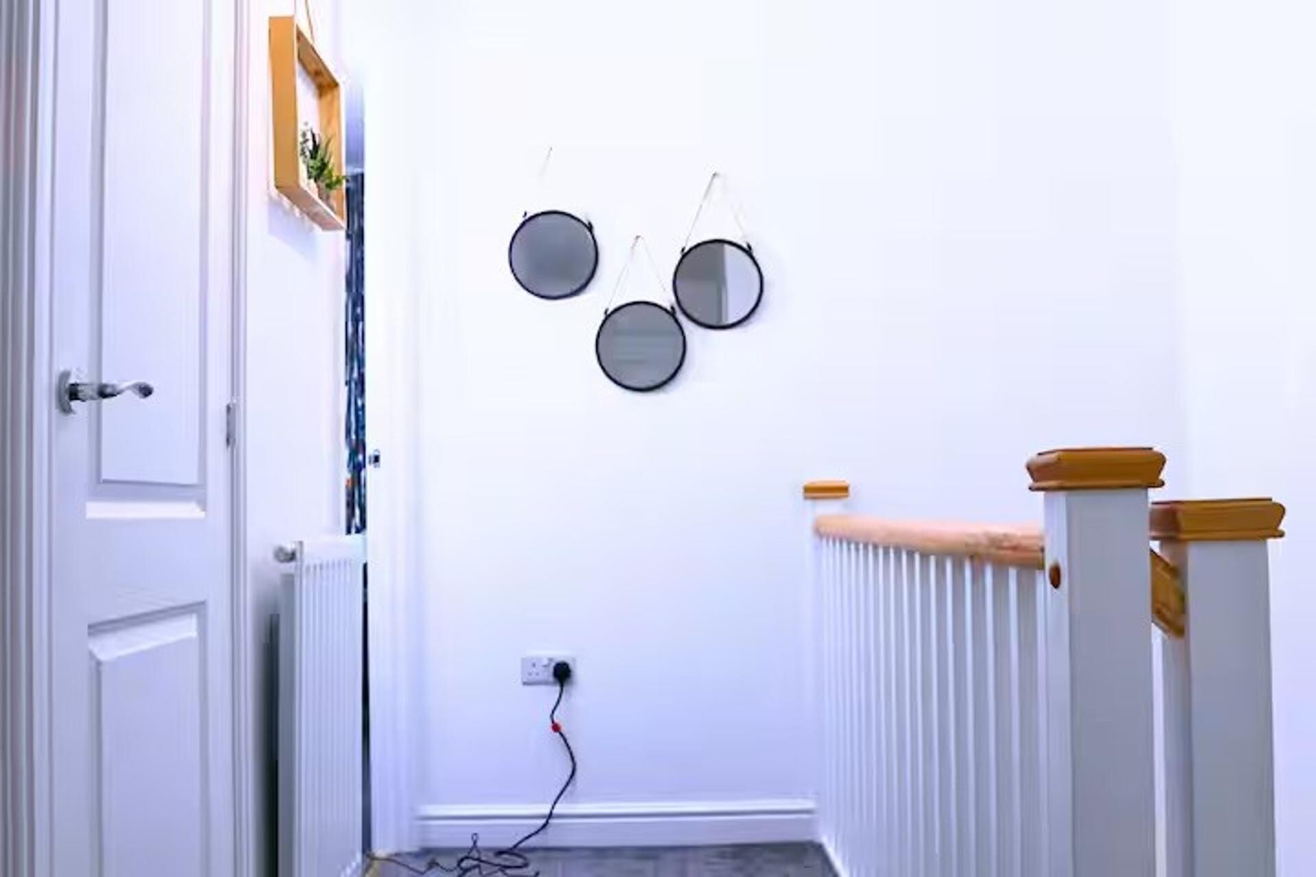 Un couloir avec une porte blanche, une rambarde blanche surmontée d’une partie en bois, et trois miroirs ronds accrochés au mur.