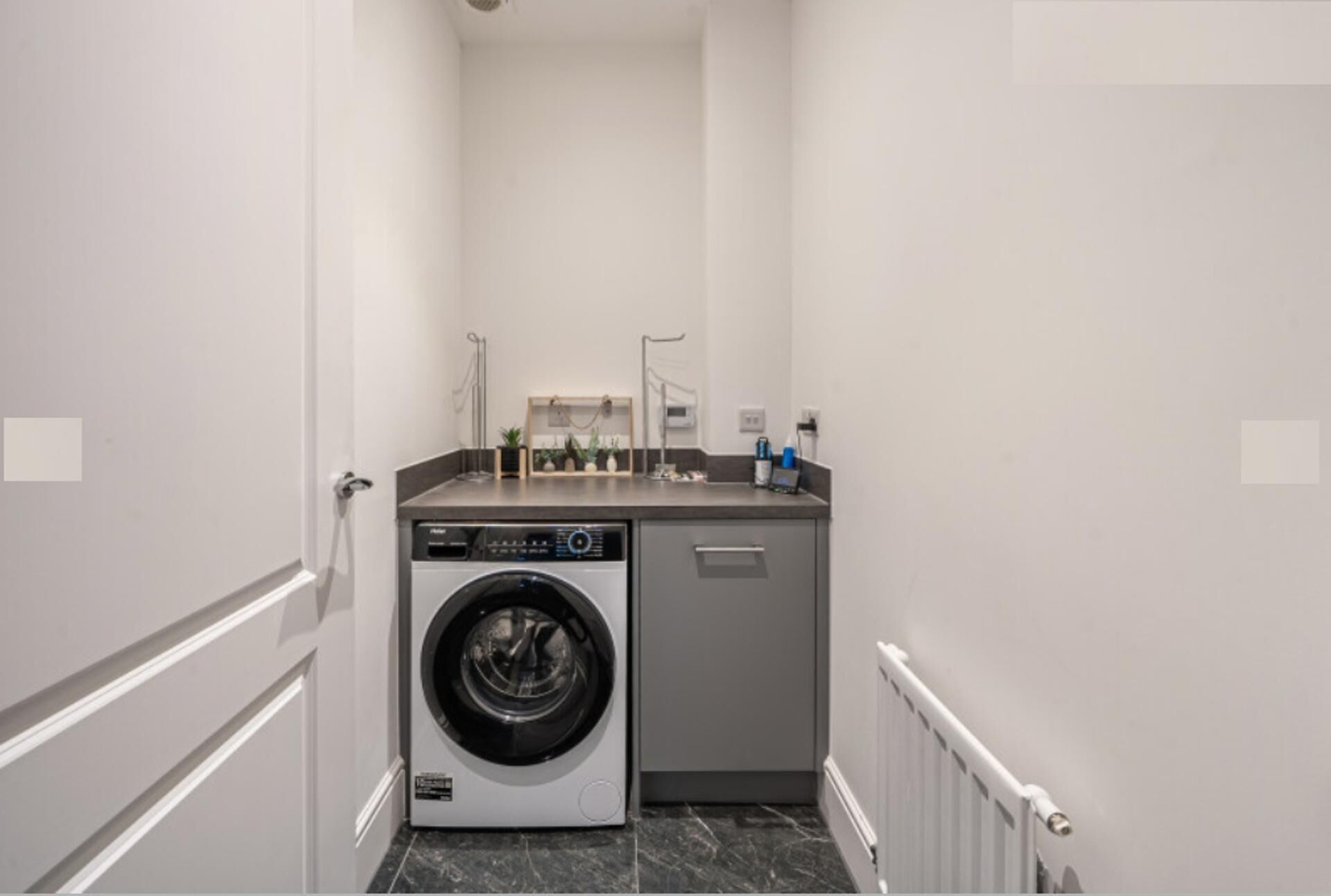 A compact laundry room with a front-loading washing machine and a small countertop with a sink and storage.