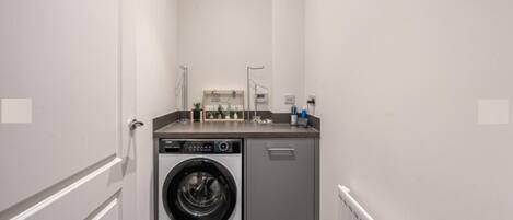 A compact laundry room with a front-loading washing machine and a small countertop with a sink and storage.