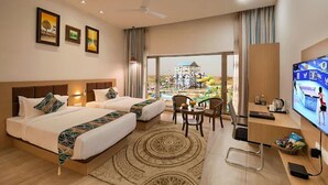 A hotel room with two beds, a desk, a TV, and a view of a building through large windows. - The Sky Imperial Chotila (Chotila)