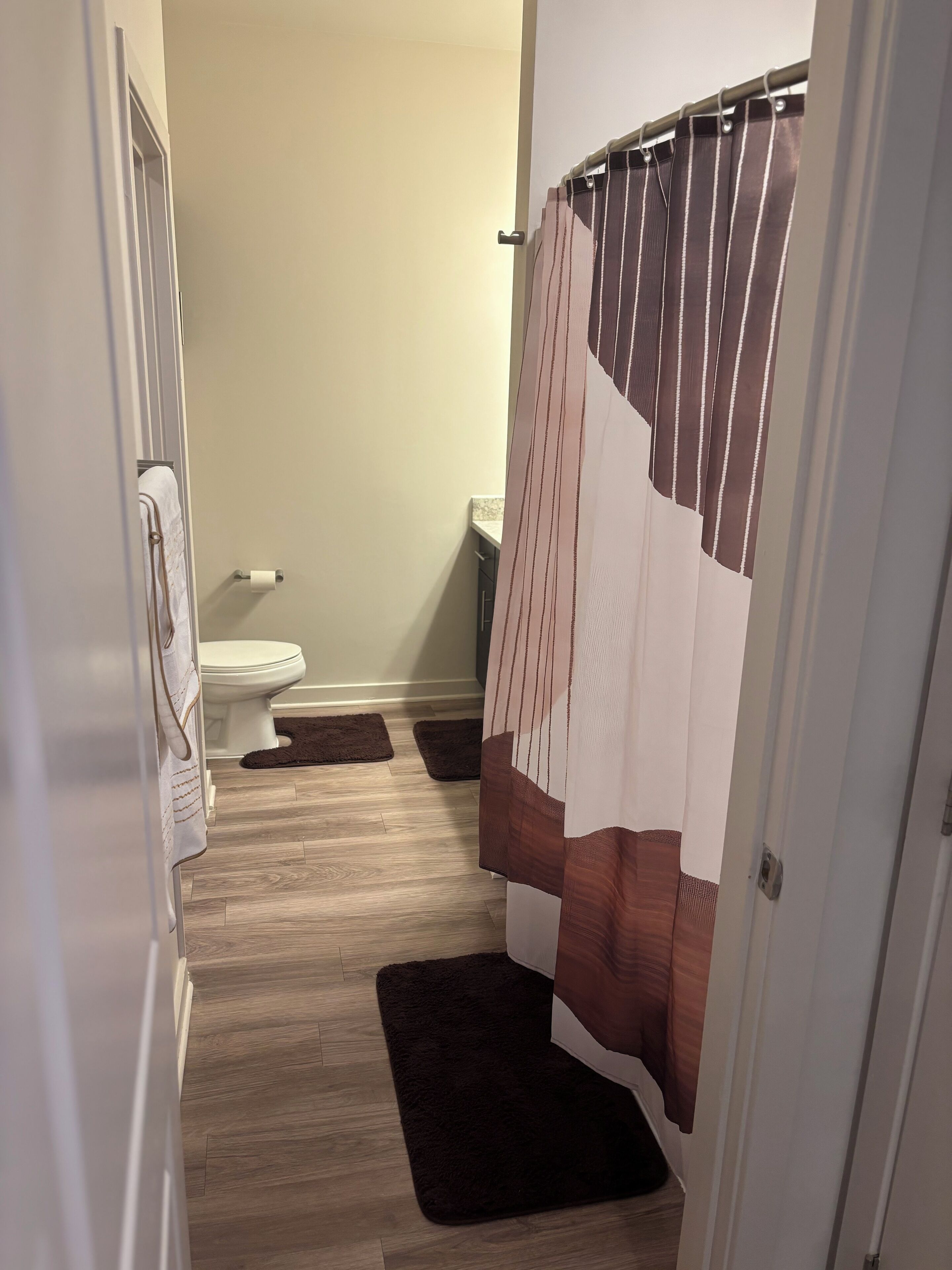 Un baño con inodoro, cortina de ducha y dos alfombras marrones oscuras en el suelo.