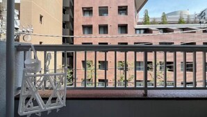 Un balcón con barandilla de metal, un colgante de luz y vista a un edificio de varios pisos con fachada de ladrillo.
