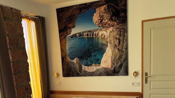 A bedroom with a large bed, a painting of a coastal scene, a brick wall, and a door. - Very pleasant apartment with sea and mountain views, boat trip (Ota)
