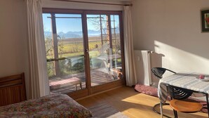 Ein Zimmer mit einem Bett, einem Tisch und Blick auf eine Landschaft durch eine Glastür.